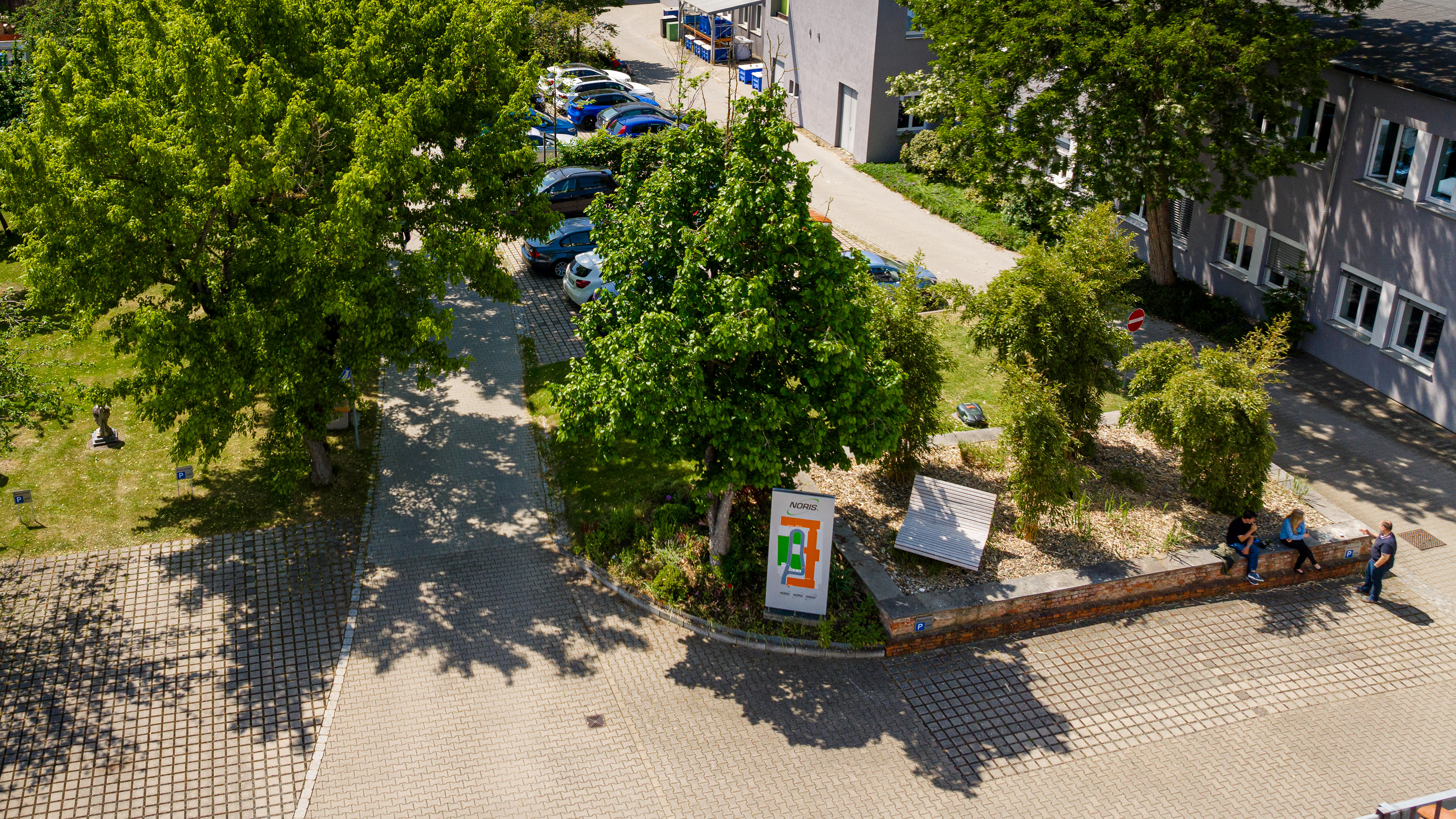 This image shows a drone view of the park of the Noris Group GmbH in Nuremberg with green tress and the company buildings.